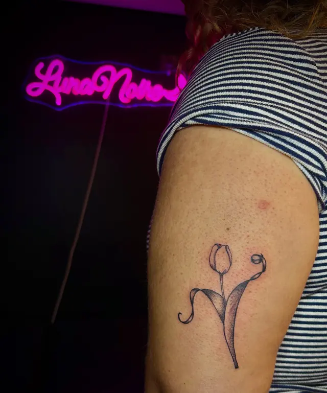Fineline tulp op de bovenarm met het roze neonbord op de achtergrond